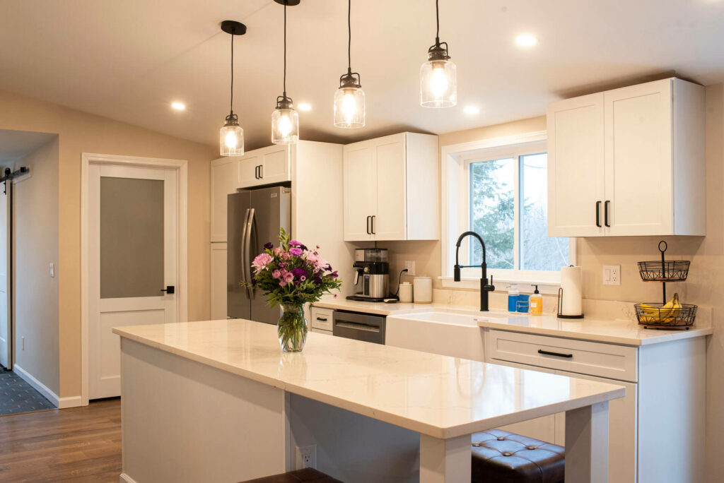 Photo of a kitchen with white cabinets and countertops, stools, lights and a sink.