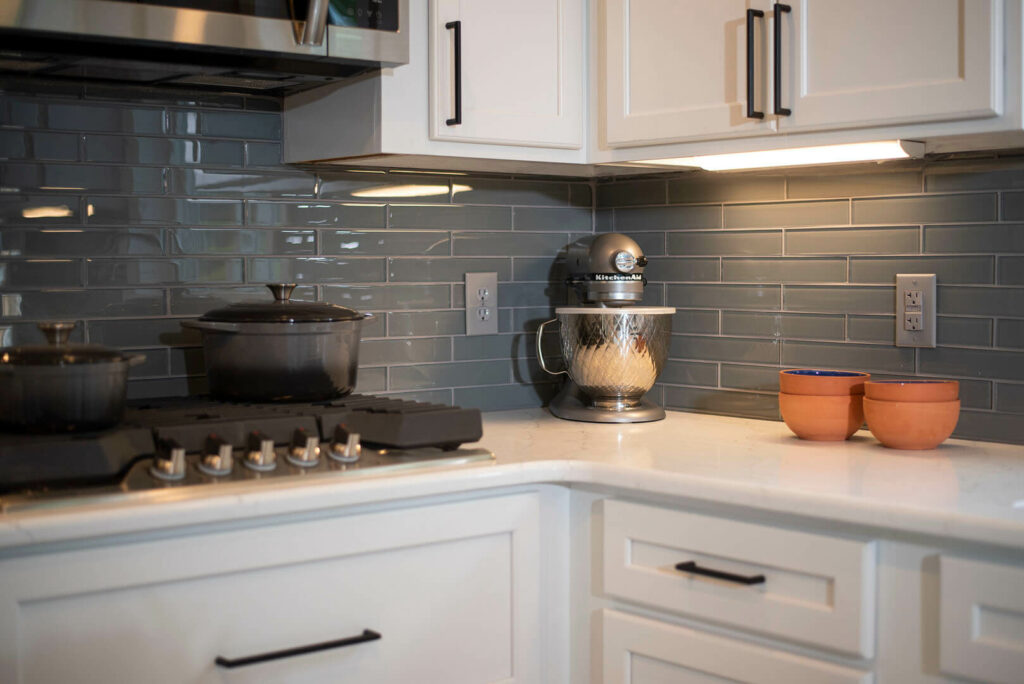 Photo of a kitchen with white countertops and cabinets and grey tile backsplash.