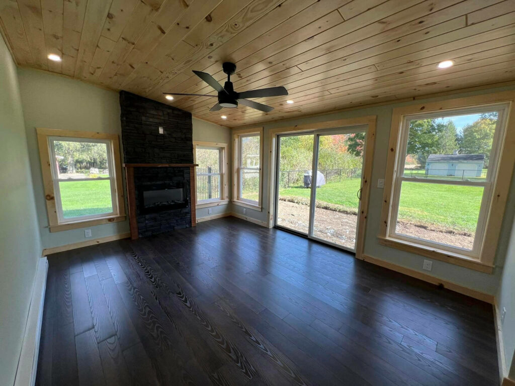 Photo of a sunroom with brown wood floors, tile fireplaces and wood ceiling.