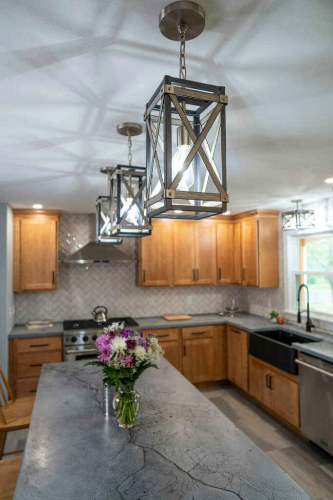 Photo of a kitchen with wood cabinets, grey marble countertops and lights.