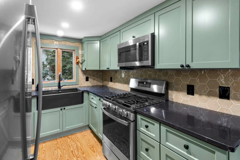 Photo of a kitchen with a black sink, marble countertops and green cabinets.