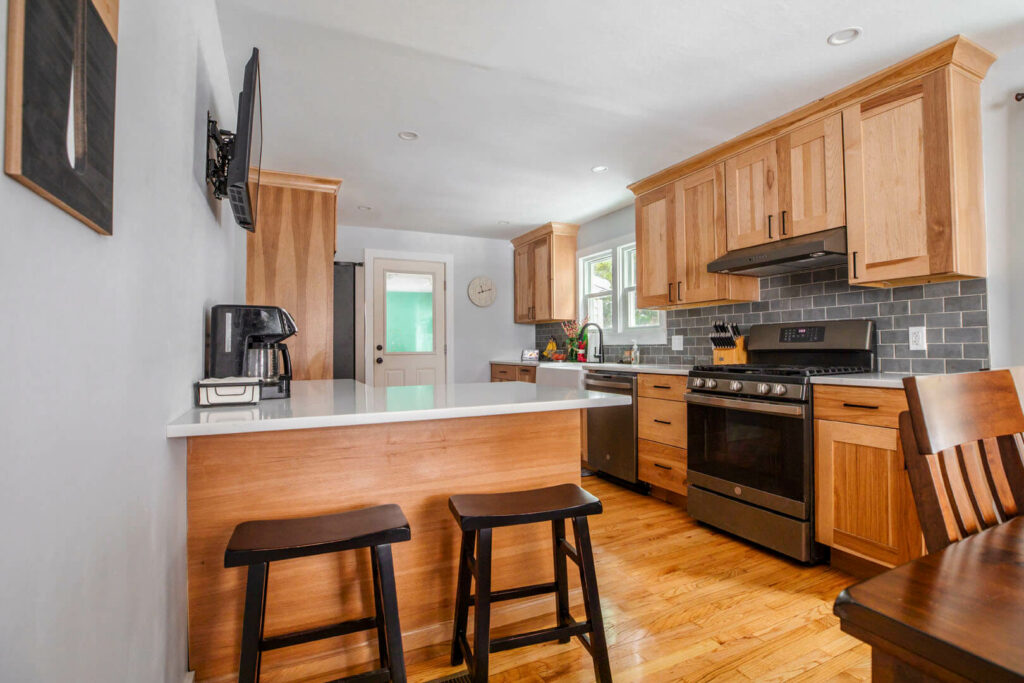 Photo of a kitchen with wood cabinets, grey backsplash, and white countertops.