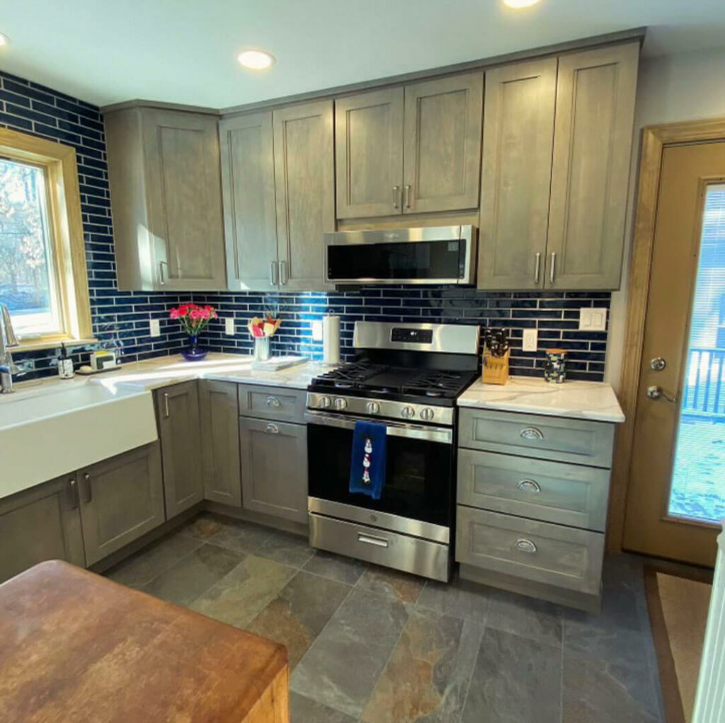 Photo of a kitchen. Including grey cabinets and stove. It also has marble countertops, a kitchen sink and tile floors.