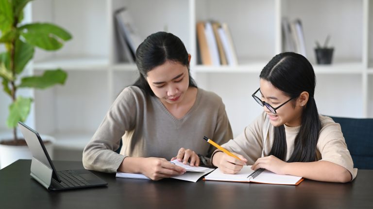 Attentive asian mother helping daughter doing homework at home