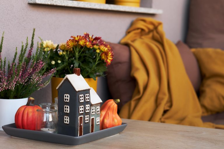 Photo of a table with two pumpkins and a small house decoration and flowers next to a couch with a yellow blanket.